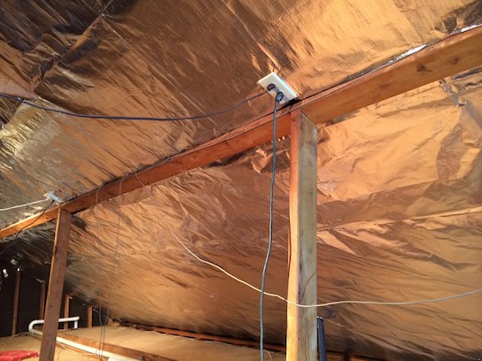 Installed radiant barrier: reflective aluminum foil stapled to the underside of roof rafters inside an attic, spanning the full slope of the roof.
